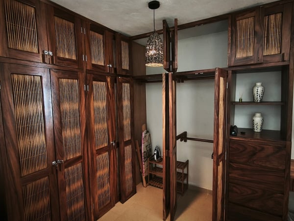 Amplio vestidor con armarios de madera oscura y paneles de bambú, lámpara artesanal y repisas decorativas