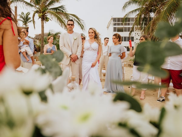 Ceremonia de boda en playa con flores blancas, palmeras tropicales e invitados en arena