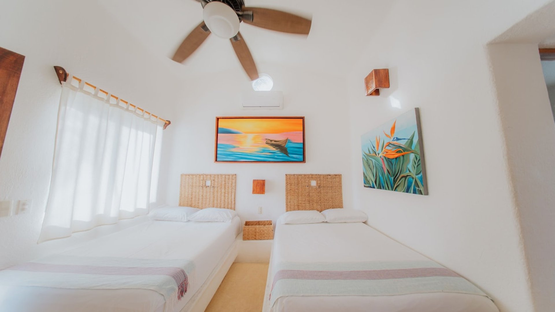 Recámara doble con dos camas individuales, cabeceras de mimbre, pinturas tropicales y ventilador de techo