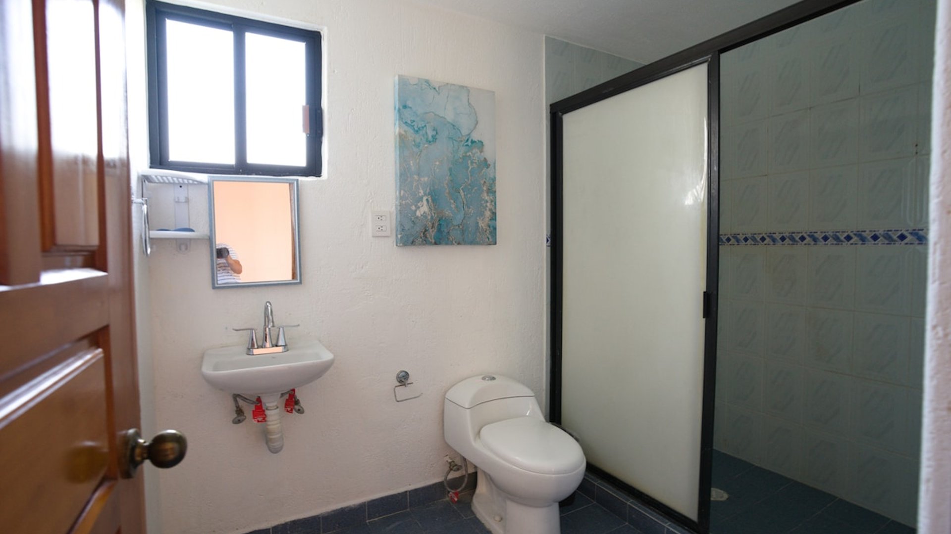 Baño completo con lavabo empotrado, inodoro blanco, cabina de ducha con puerta corrediza y cuadro decorativo en tonos azules