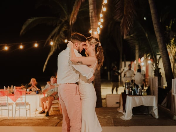 Primer baile de boda en pista bajo palmeras con luces colgantes y bar al fondo