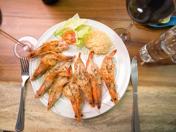 Plato de camarones a la plancha con arroz, ensalada y copas de vino sobre mesa de madera