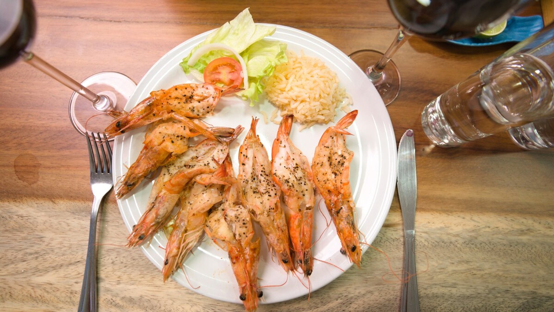 Plato de camarones a la plancha con arroz, ensalada y copas de vino sobre mesa de madera