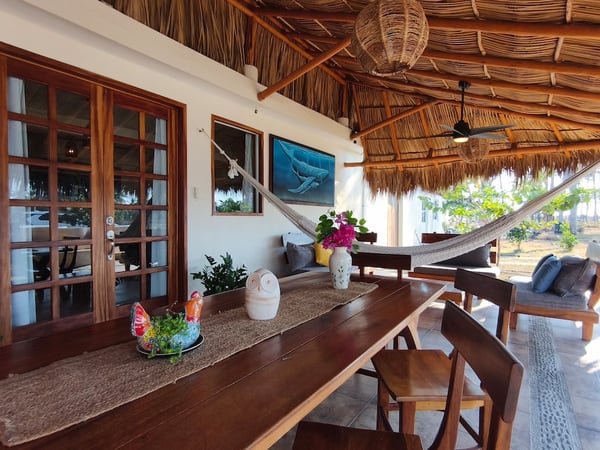 Terraza con palapa, mesa de madera, hamaca y decoración artesanal con vista al jardín y palmeras al fondo