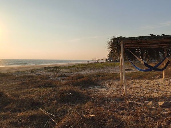 Hamaca bajo palapa rústica frente al mar al atardecer en playa de arena dorada