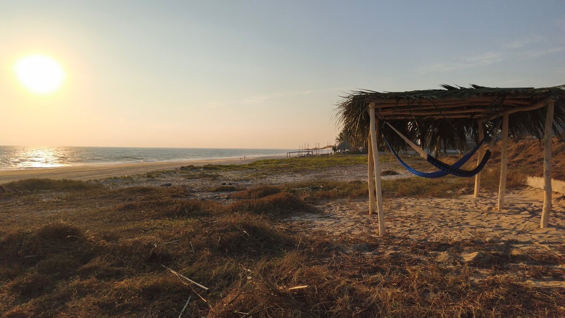 Hamaca bajo palapa rústica frente al mar al atardecer en playa de arena dorada