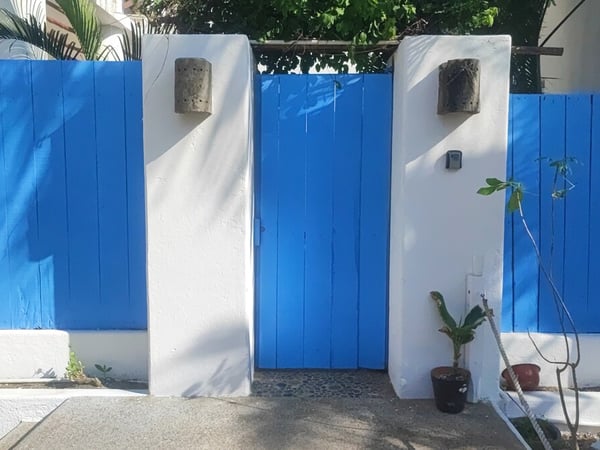 Entrada principal con barda blanca y tablones azules, portón de madera y pequeña planta en maceta
