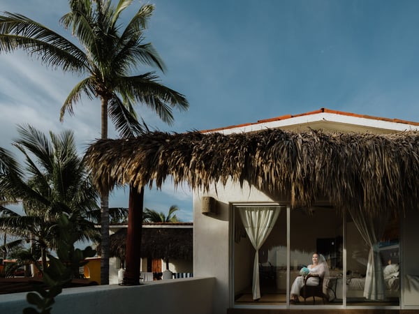 Villa frente al mar con palapa de palma y palmeras bajo cielo azul en ambiente tropical playero