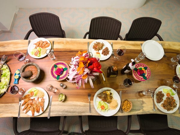 Vista cenital de mesa de madera maciza con banquete de mariscos, pescado, camarones, salsas y centro floral colorido