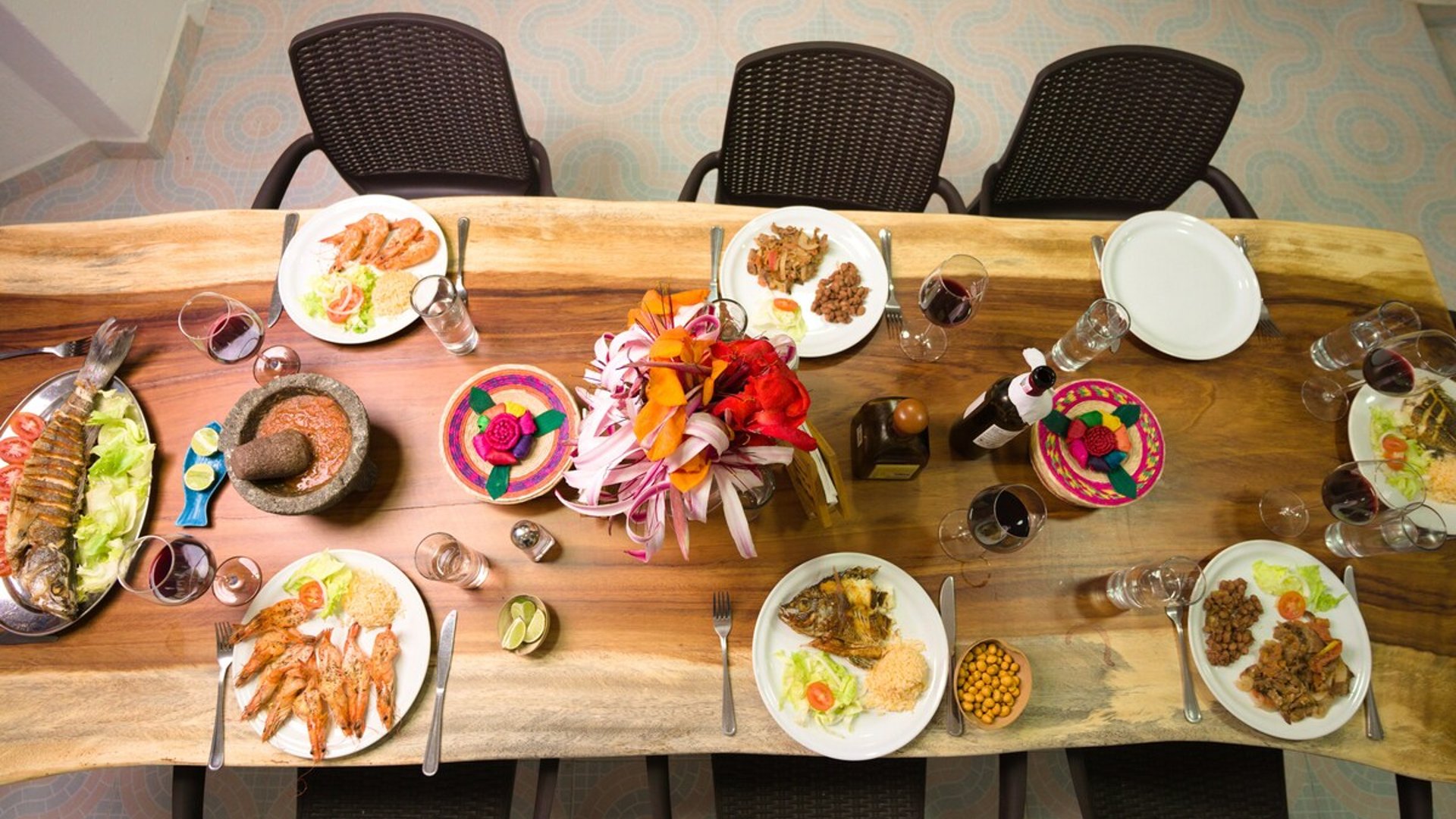 Vista cenital de mesa de madera maciza con banquete de mariscos, pescado, camarones, salsas y centro floral colorido
