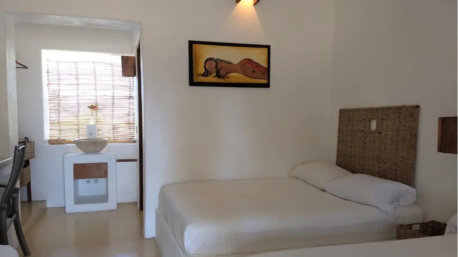 Habitación doble con camas individuales, cabeceras de mimbre, paredes blancas y pintura tropical en ambiente cálido