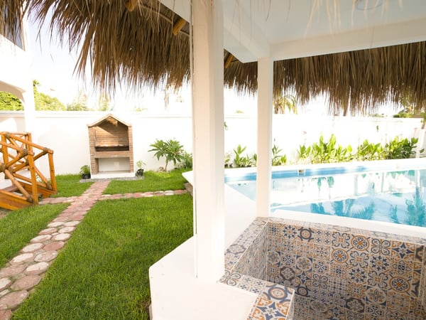 Jardín con pasto verde, asador de ladrillo, jacuzzi con mosaicos talavera y alberca bajo palapa en área exterior