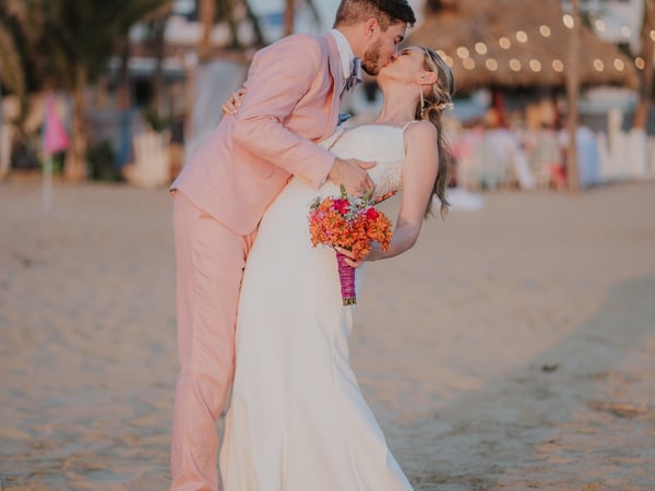Boda en playa con villa frente al mar, palmeras y luces colgantes al atardecer