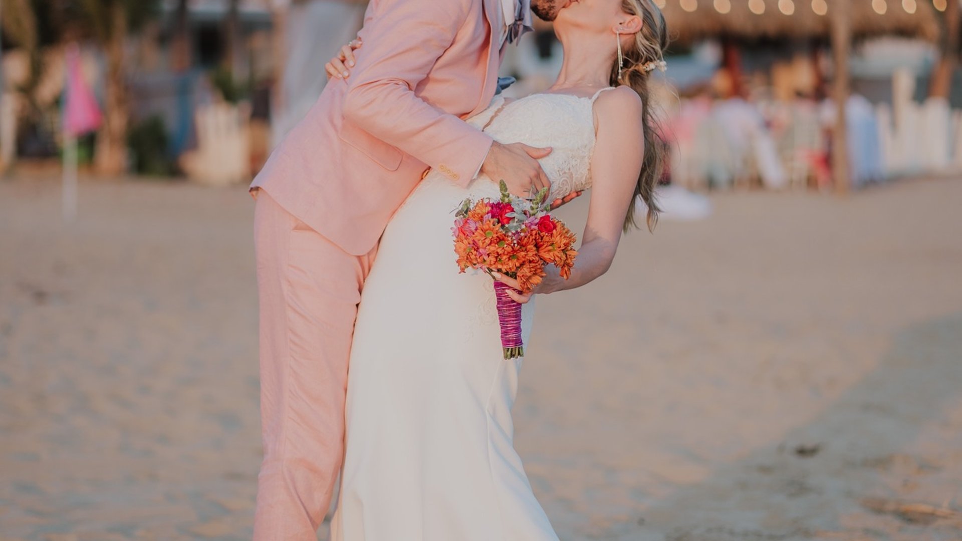 Boda en playa con villa frente al mar, palmeras y luces colgantes al atardecer