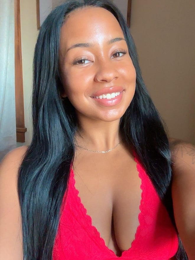 A smiling woman with long dark hair wearing a bright red top indoors.