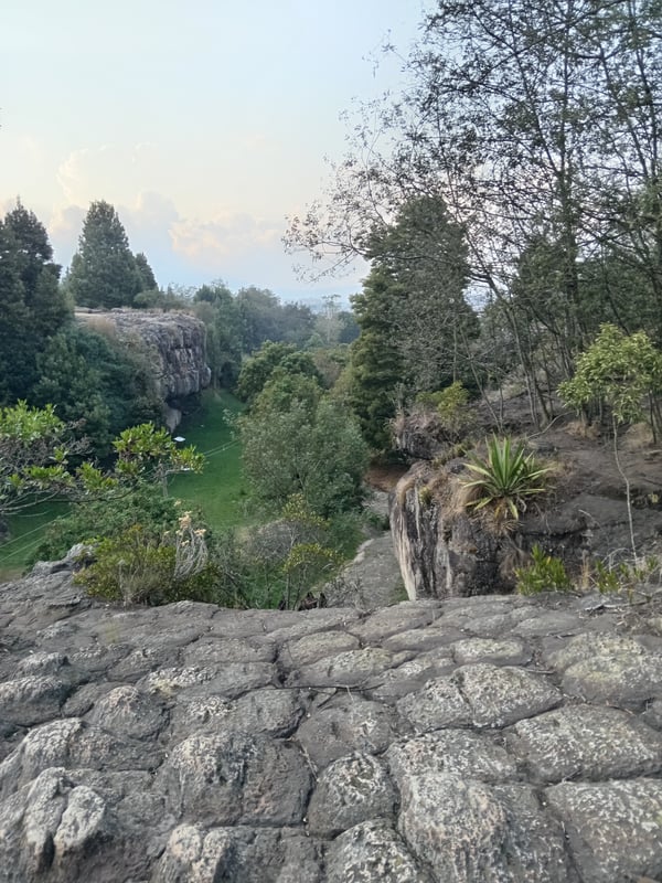 Scenic landscape view of lush green cliffs, trees, and a valley during sunset.