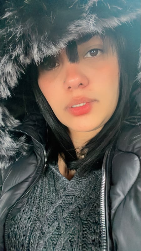 Young woman with dark hair wearing a fur-lined hooded jacket, smiling softly at the camera.