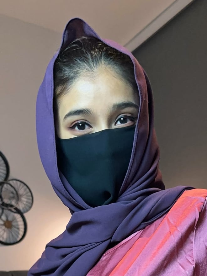 A person wearing a purple headscarf and black face covering, looking directly at the camera.
