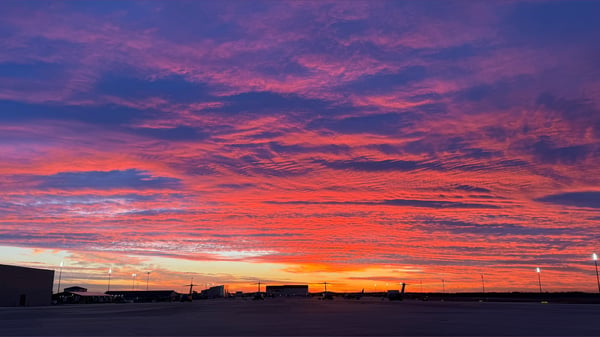 Vibrant sunset sky with orange and purple hues over a parking lot and distant buildings.