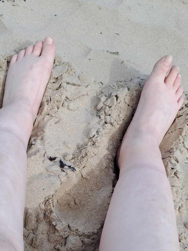 Close-up of bare feet on a sandy beach with waves in the background.