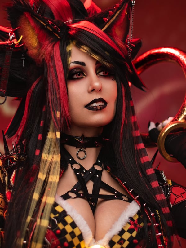 Cosplayer in a detailed red and black fantasy outfit with fox ears, heavy makeup, and dramatic accessories.
