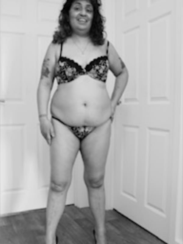 Black and white photo of a woman posing in lingerie against a bedroom door.