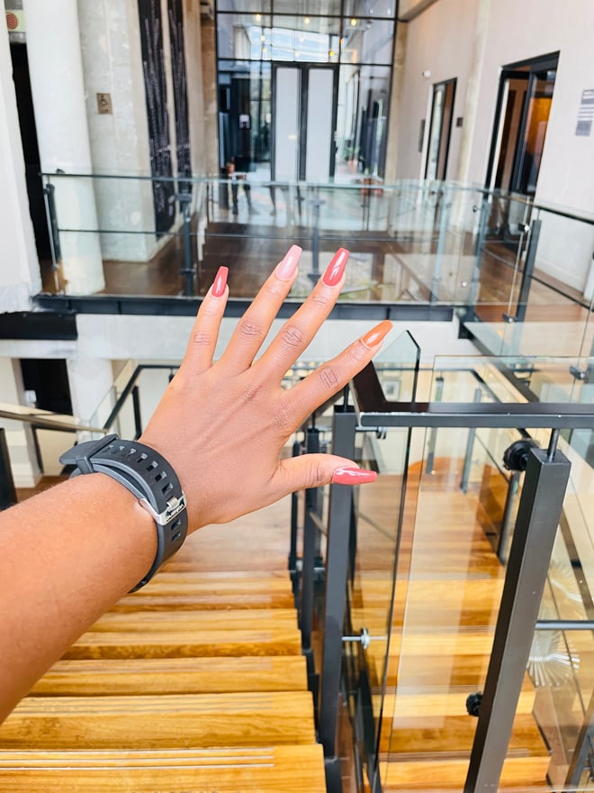 Hand with colorful manicured nails extended towards the camera in a modern glass-walled building interior with staircases.
