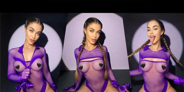 A woman with long braided hair posing confidently in a sheer purple outfit with gloves against a purple spotlight background.