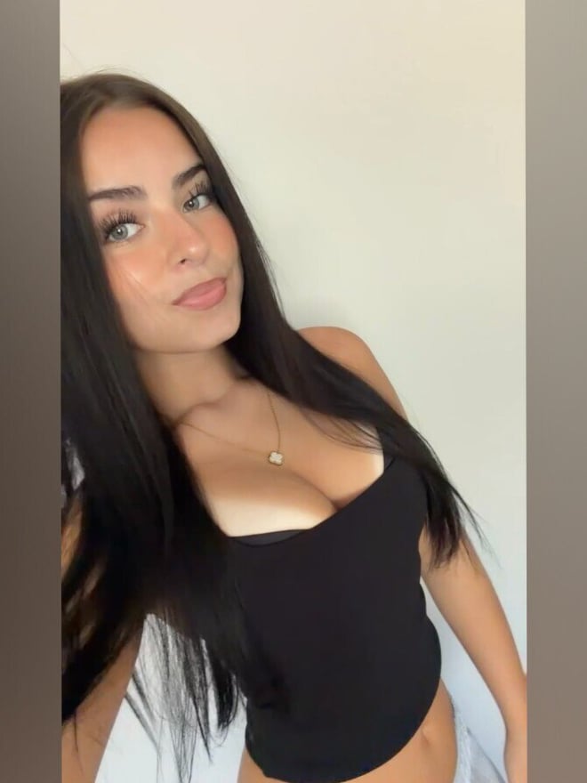 A woman with long dark hair posing indoors in a black outfit.