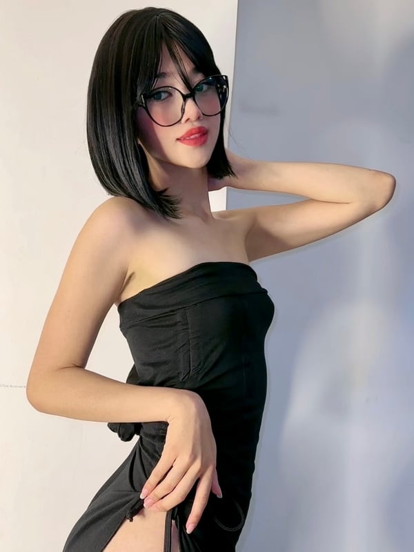 A person with long brown hair wearing a black lace top, posing indoors.