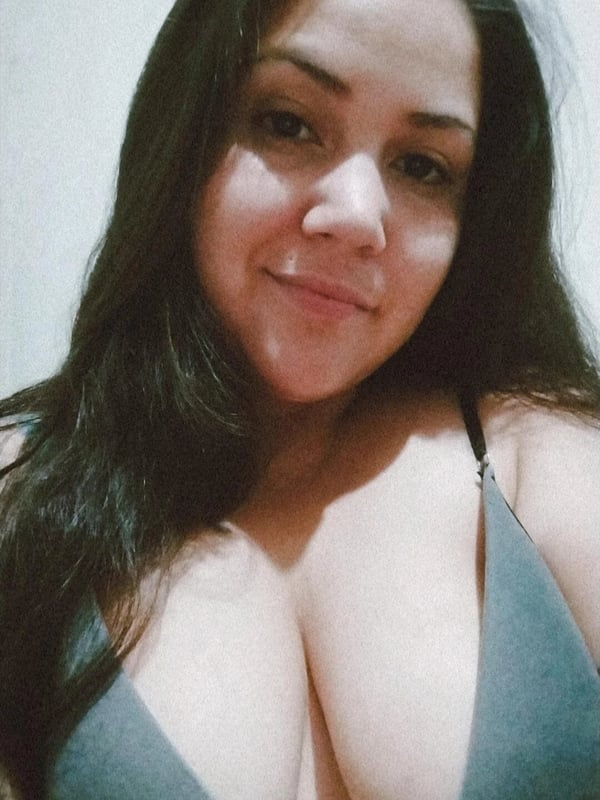 A woman with long dark hair smiling at the camera, wearing a gray swimsuit top.