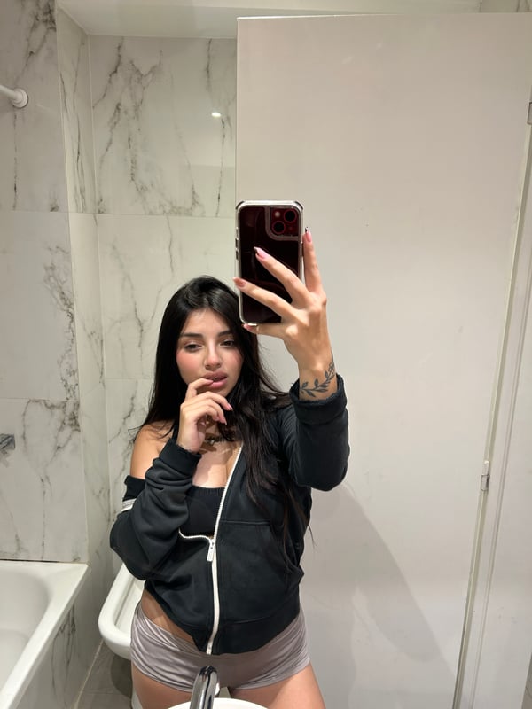 A person posing in a bedroom setting while holding a phone.