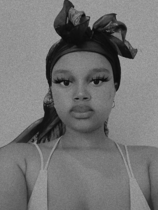 Close-up portrait of a woman with a headwrap, wearing thin straps, in black and white filter.