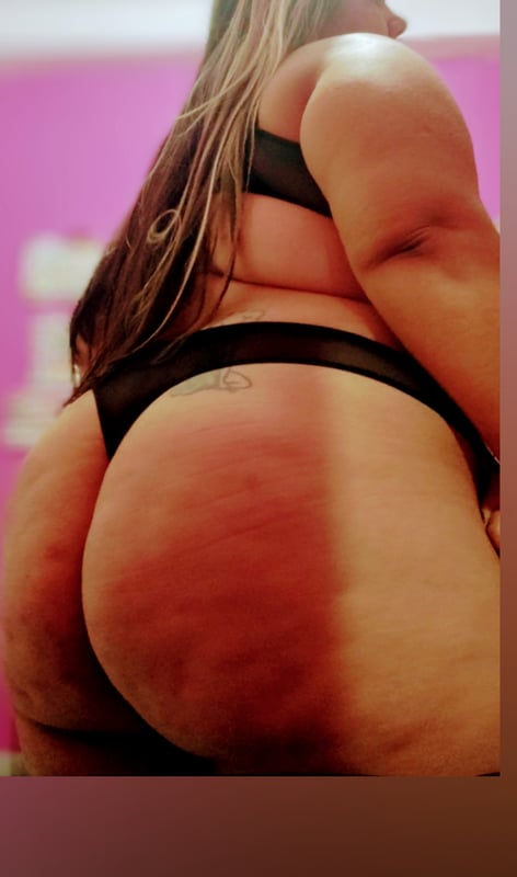 A woman posing from behind in black lingerie against a pink background.
