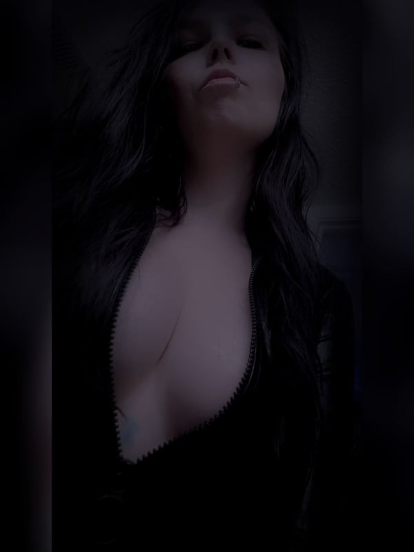 Close-up portrait of a woman with long dark hair, pale skin, and dark lipstick, gazing with a mysterious expression in dim lighting.