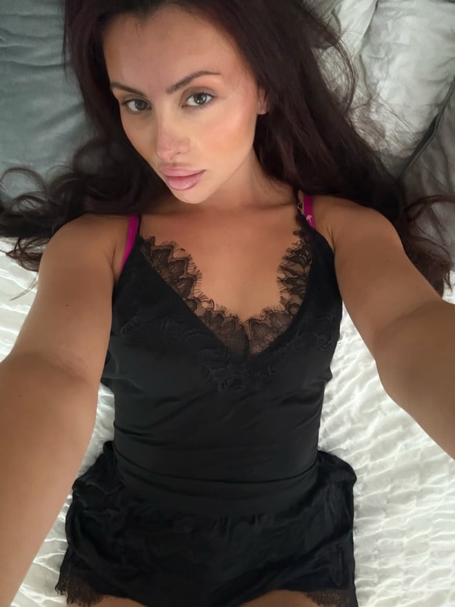 A woman with long dark hair takes a mirror selfie in a bedroom while wearing colorful attire.