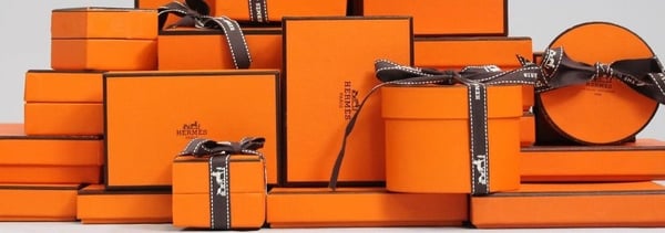 Arrangement of orange luxury gift boxes with ribbons and branding on a neutral background.