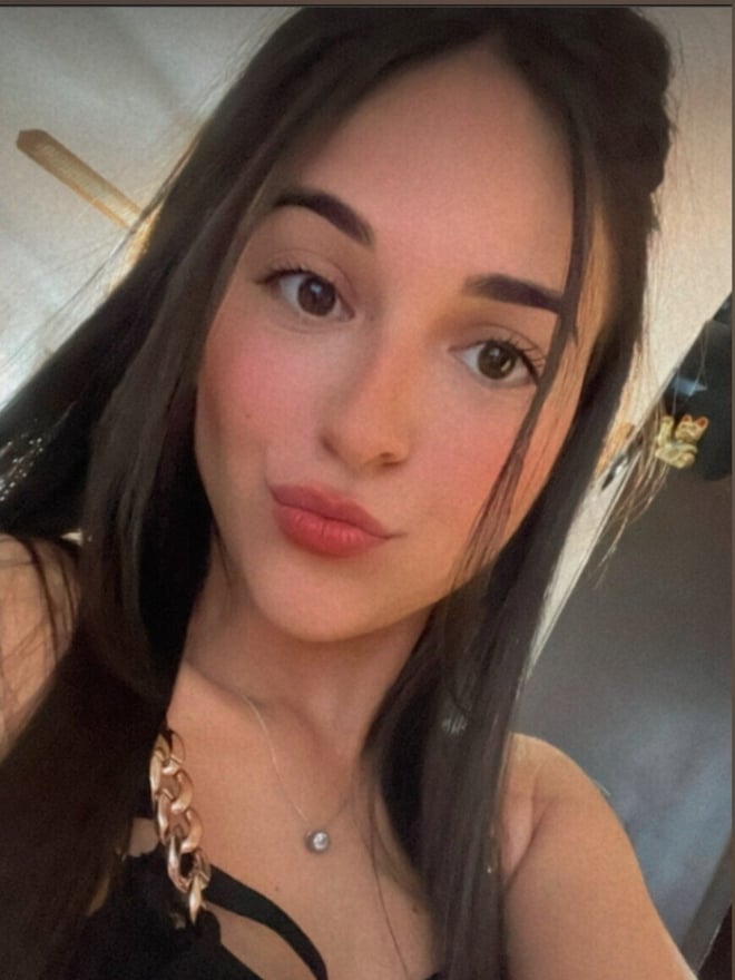 Close-up portrait of a young woman with long dark hair wearing a black top and necklace.