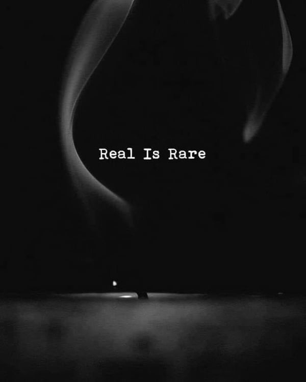 Artistic black and white image featuring swirling smoke shapes with the text 'Real Is Rare' overlaid.