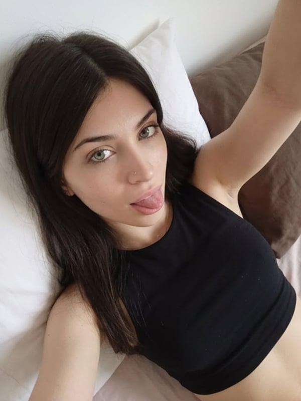 A young woman with long dark hair and green eyes looks at the camera, wearing a blue top in an indoor setting.