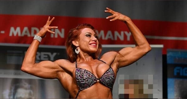 Muscular woman flexing her biceps on stage during a fitness competition, wearing a colorful bikini top.