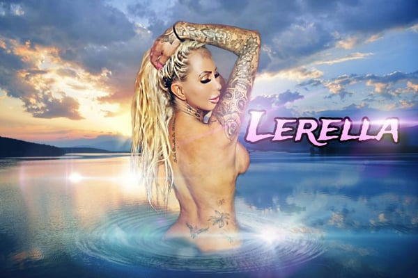 A woman with long blonde hair and tattoos poses confidently by a scenic lakeside at sunset, with water and sky in the background.