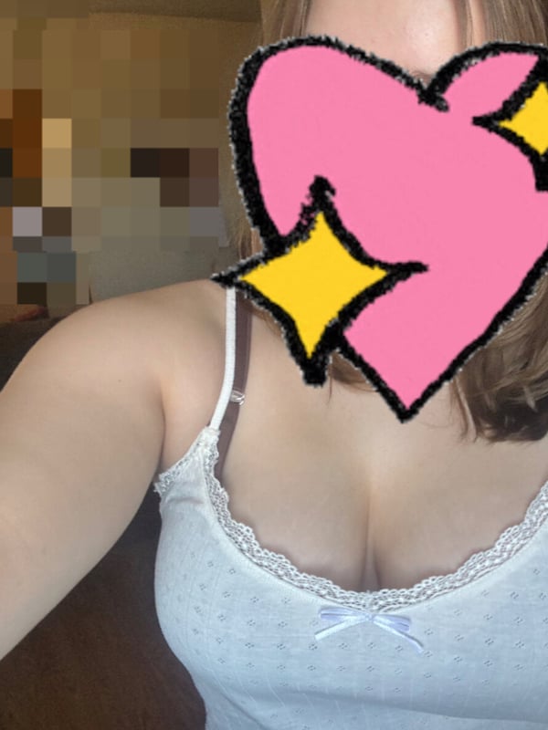Close-up selfie of a woman in a lace-trimmed top, with a large pink heart covering her face and yellow stars, in a casual indoor setting.
