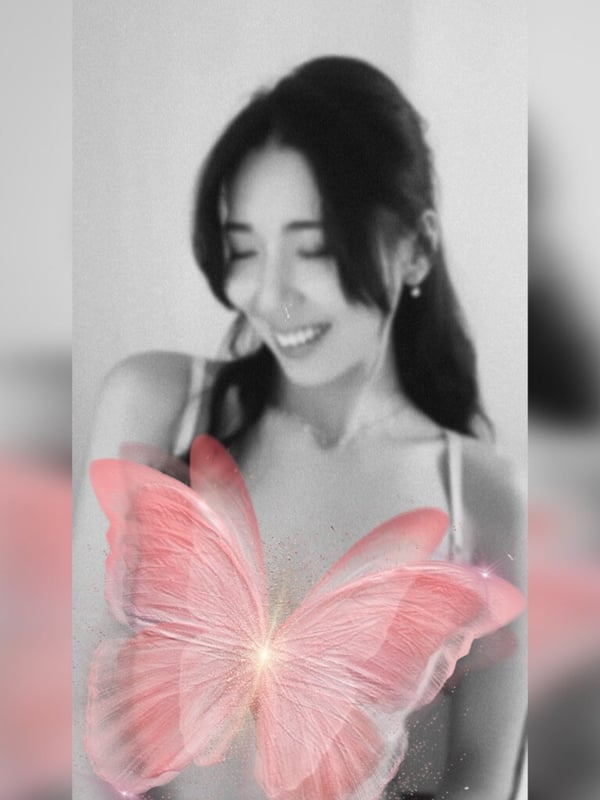 A smiling young woman with long dark hair in a black-and-white portrait, overlaid with glowing pink butterfly wings.