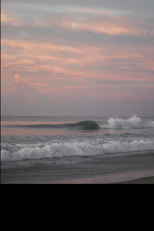 Scenic ocean view at sunset with waves crashing on the shore under a colorful sky.