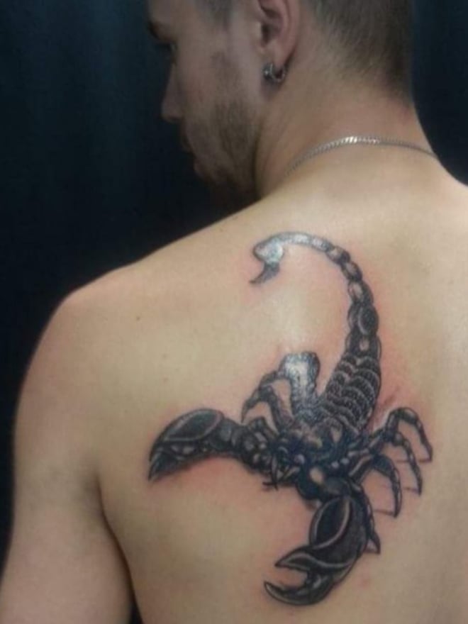 Close-up of a man's upper back showing a detailed black scorpion tattoo, with short hair and an earring visible.
