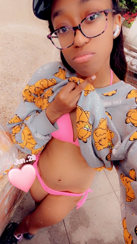 Young woman wearing glasses, a cap, and a colorful swimsuit top with an open patterned cover-up, posing confidently outdoors.