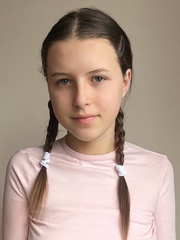 Close-up portrait of a young woman with brown hair styled in braids, wearing a pink top, gazing at the camera with a gentle expression.