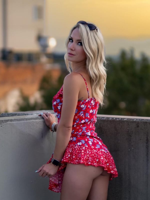 A woman in a red floral dress leaning against a balcony railing at sunset.