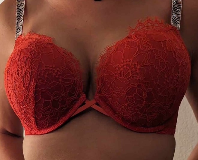 Woman posing in a red lace bra with intricate detailing against a plain background.